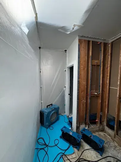 Plastic containment and air movers drying an opened wall cavity inside a home