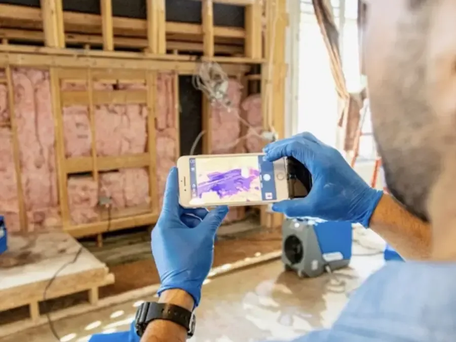 Technician scanning open wall framing with a thermal camera to map where moisture is still trapped
