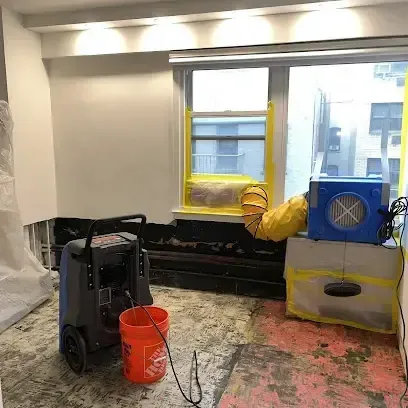 A dehumidifier and an air mover running in a room where the wet flooring has already been taken up for drying