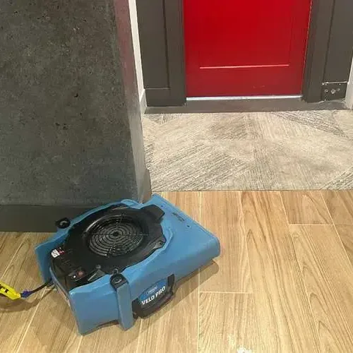 An air mover blowing across a wood-look tile floor next to an open doorway during a dry-out