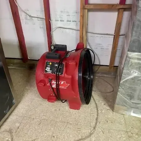 Red air mover drying a room where the lower wall was opened and plastic sheeting hangs