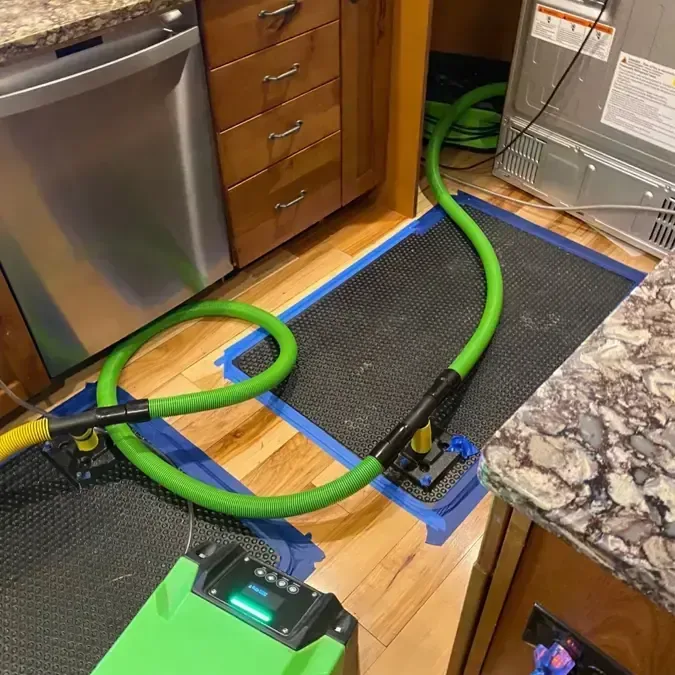 Drying mat and hose set on hardwood in front of a leaking kitchen dishwasher