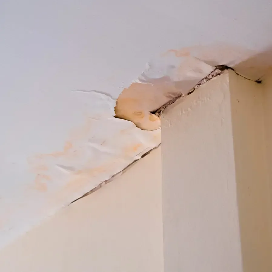 Stained ceiling drywall cracking and peeling at a corner after a leak from above