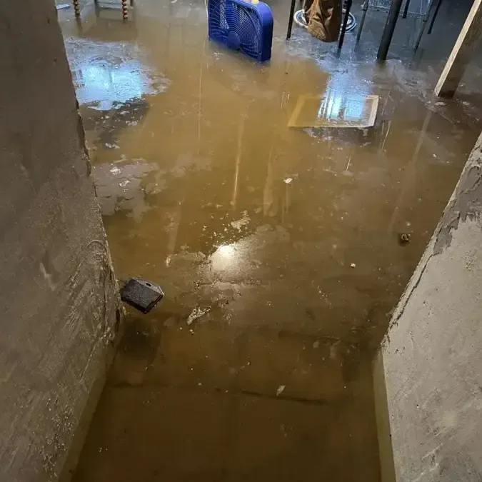 Muddy storm water standing across a flooded floor at the foot of a stairway