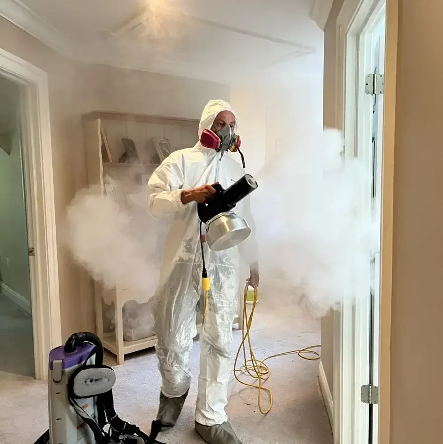 Technician in a protective suit and respirator fogging antimicrobial down a hallway