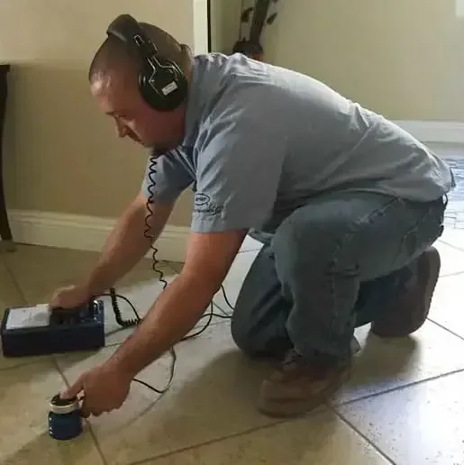 Technician using acoustic leak detection gear on a tile floor laid over a concrete slab
