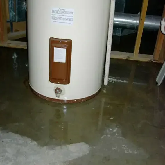 Tank water heater sitting in a puddle that has spread across the floor